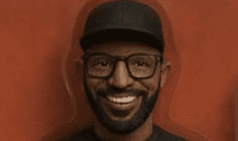 Man smiling with glasses and cap.